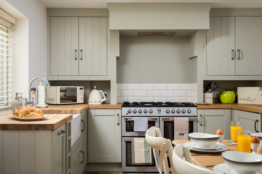 This is an example of a mid-sized country u-shaped eat-in kitchen in Gloucestershire with a farmhouse sink, recessed-panel cabinets, grey cabinets, wood benchtops, stainless steel appliances and brown benchtop.