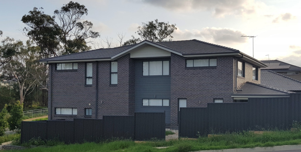 Large contemporary two-storey brick grey house exterior in Sydney with a hip roof and a tile roof.