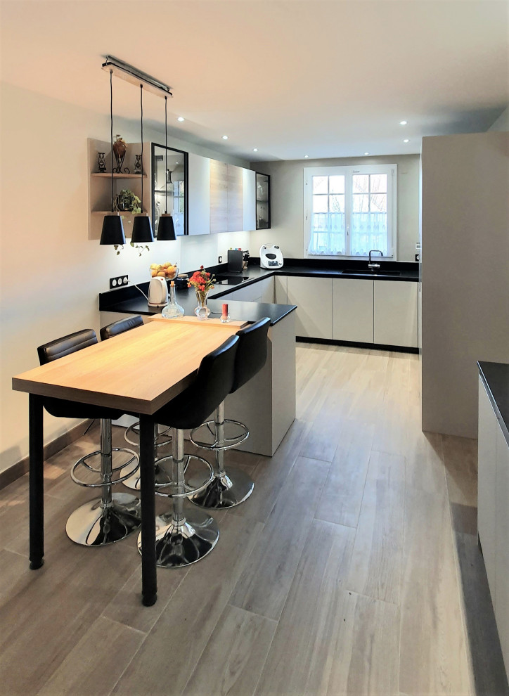 Photo of a mid-sized modern single-wall open plan kitchen in Other with laminate floors, beige floor, an undermount sink, flat-panel cabinets, white cabinets, granite benchtops, black splashback, granite splashback, panelled appliances, with island and black benchtop.