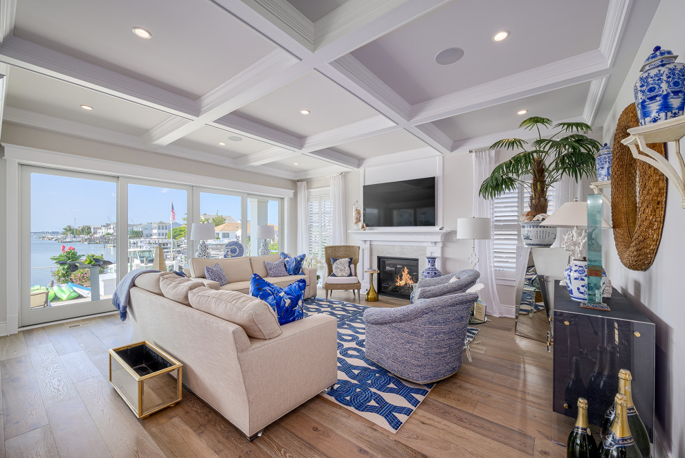 Design ideas for a beach style living room in Philadelphia with beige walls, medium hardwood floors, a standard fireplace, a stone fireplace surround, a wall-mounted tv, brown floor and coffered.