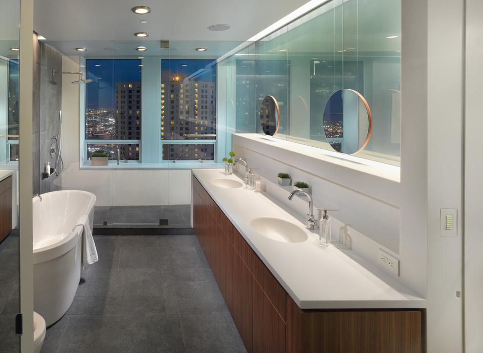 This is an example of a mid-sized contemporary master bathroom in San Francisco with a freestanding tub, flat-panel cabinets, dark wood cabinets, an alcove shower, white walls, engineered quartz benchtops, grey floor, a hinged shower door and white benchtops.