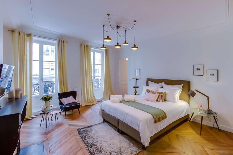 Photo of a large scandinavian master bedroom in Paris with white walls, light hardwood floors, a standard fireplace and a stone fireplace surround.