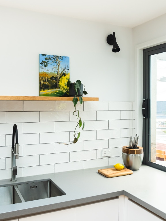 Small contemporary u-shaped kitchen pantry in Melbourne with a built-in sink, flat-panel cabinets, white cabinets, composite countertops, white splashback, metro tiled splashback, stainless steel appliances, no island and grey worktops.