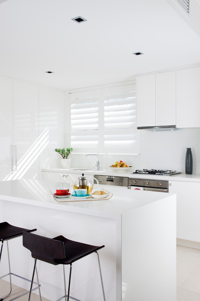 Photo of a beach style kitchen in Sydney with white cabinets, flat-panel cabinets and with island.