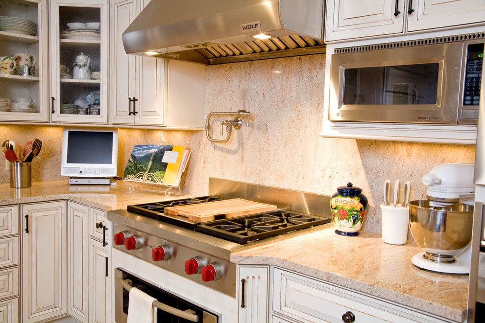 Example of a large transitional l-shaped light wood floor kitchen design with a farmhouse sink, raised-panel cabinets, beige cabinets, granite countertops, beige backsplash, stone slab backsplash, paneled appliances and an island