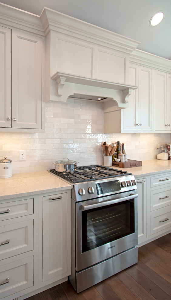 Example of a transitional medium tone wood floor, brown floor and vaulted ceiling eat-in kitchen design with shaker cabinets, white cabinets, quartz countertops, white backsplash, ceramic backsplash, stainless steel appliances and white countertops