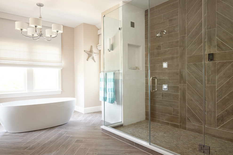 Photo of a large beach style master bathroom in New York with a freestanding tub, an alcove shower, a one-piece toilet, brown tile, porcelain tile, beige walls, porcelain floors, brown floor and a hinged shower door.