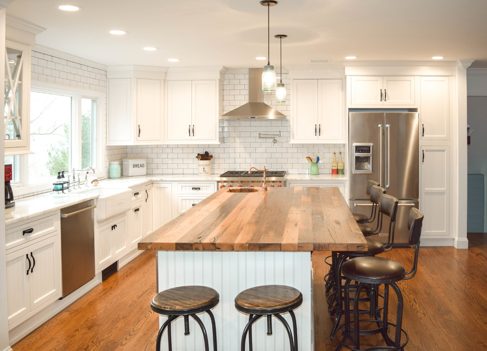 Design ideas for a large country l-shaped eat-in kitchen in New York with a farmhouse sink, beaded inset cabinets, white cabinets, wood benchtops, white splashback, subway tile splashback, stainless steel appliances, medium hardwood floors and with island.