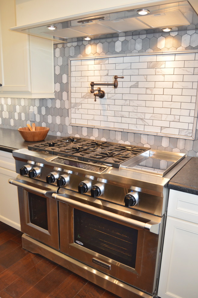 Mid-sized transitional u-shaped medium tone wood floor enclosed kitchen photo with a farmhouse sink, recessed-panel cabinets, white cabinets, solid surface countertops, gray backsplash, ceramic backsplash, stainless steel appliances and an island
