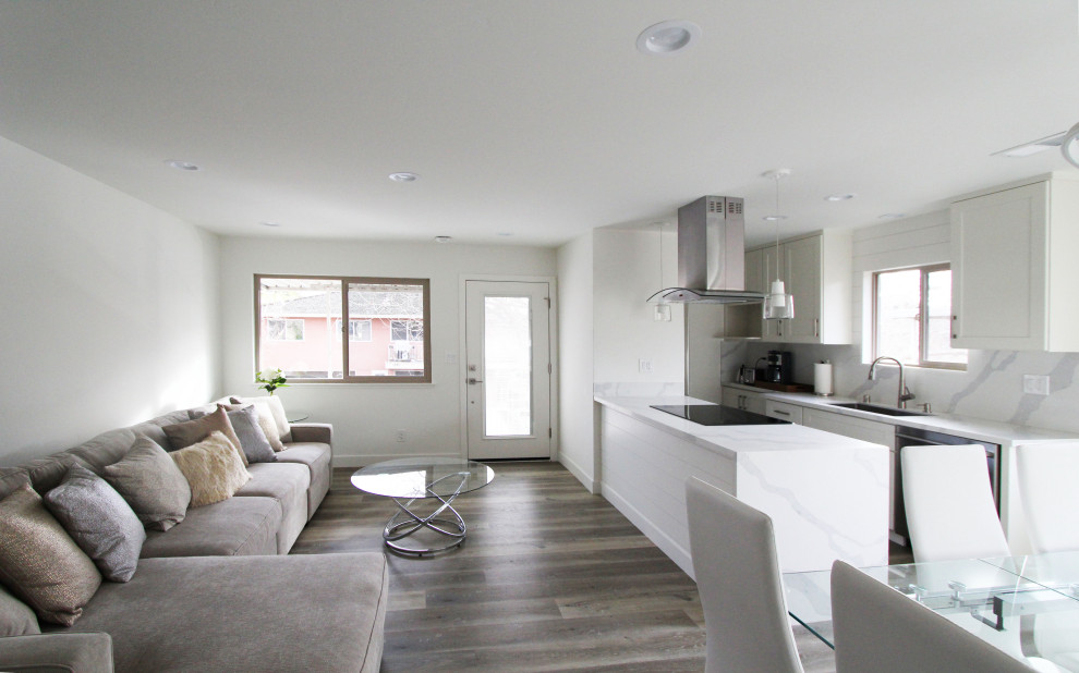 Example of a small galley vinyl floor and brown floor open concept kitchen design with an undermount sink, shaker cabinets, white cabinets, quartz countertops, white backsplash, quartz backsplash, stainless steel appliances, a peninsula and white countertops