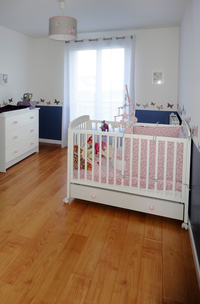 Design ideas for a mid-sized traditional nursery for girls in Paris with multi-coloured walls and light hardwood floors.