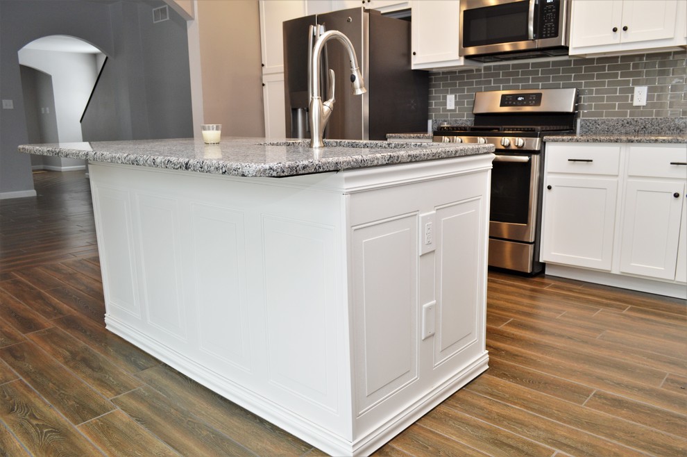 This is an example of a large transitional l-shaped eat-in kitchen in Chicago with an undermount sink, shaker cabinets, white cabinets, granite benchtops, grey splashback, ceramic splashback, with island and grey benchtop.