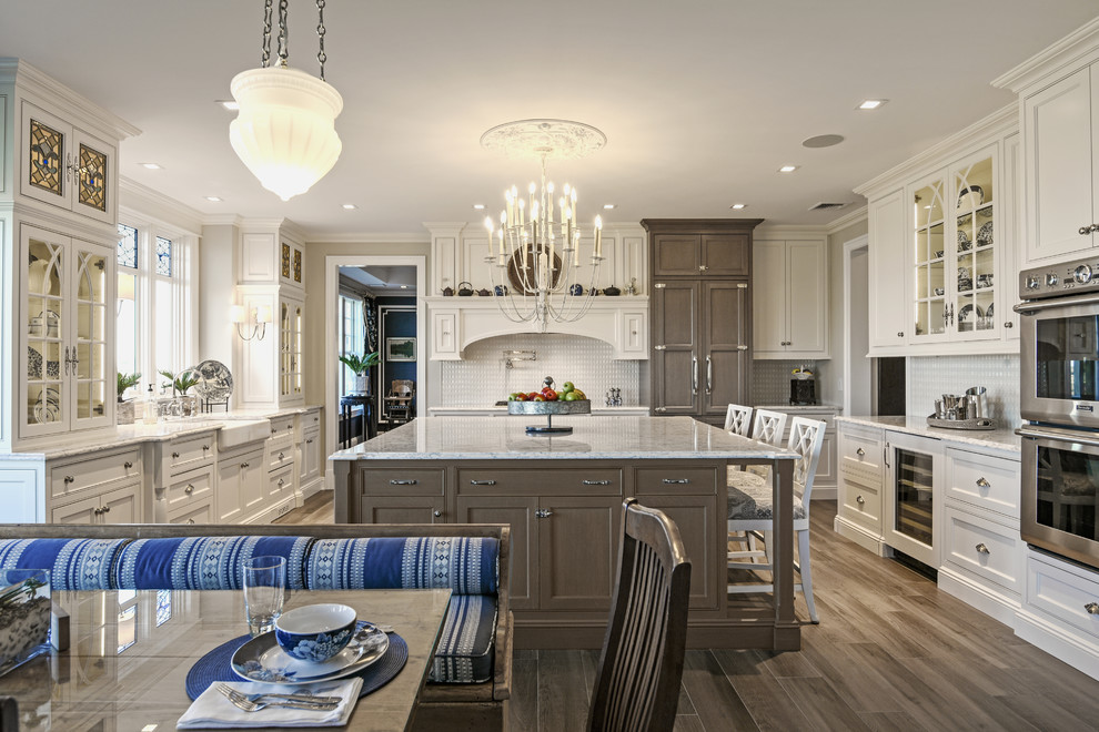 Traditional u-shaped eat-in kitchen in New York with a farmhouse sink, beaded inset cabinets, white cabinets, white splashback, stainless steel appliances, dark hardwood floors, with island and brown floor.