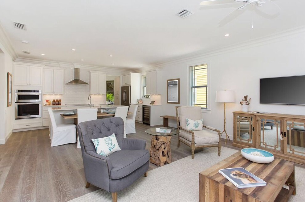 This is an example of a large beach style open concept family room in Tampa with white walls, light hardwood floors, no fireplace and a wall-mounted tv.