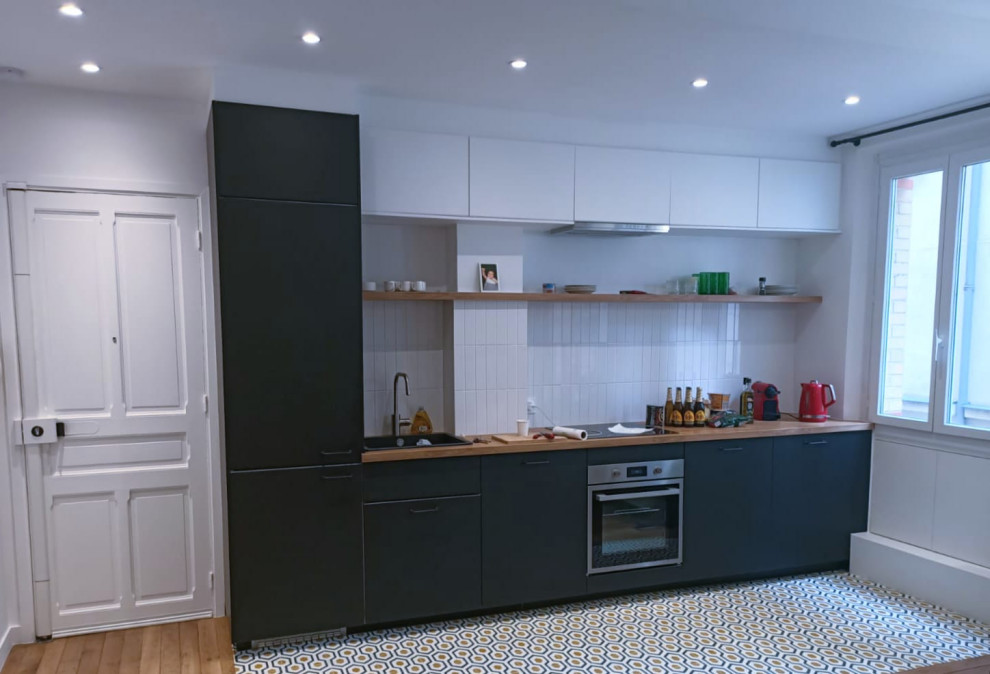 Mid-sized traditional single-wall open plan kitchen in Paris with an integrated sink, flat-panel cabinets, black cabinets, laminate benchtops, white splashback, subway tile splashback, panelled appliances, cement tiles, no island, yellow floor and brown benchtop.