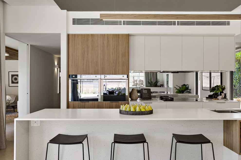 Design ideas for a mid-sized contemporary single-wall eat-in kitchen in Canberra - Queanbeyan with an undermount sink, flat-panel cabinets, white cabinets, quartz benchtops, metallic splashback, mirror splashback, black appliances, concrete floors, with island, grey floor and white benchtop.