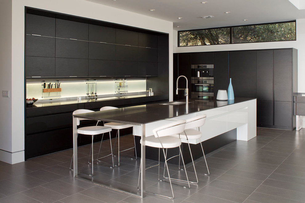 Large contemporary l-shaped open plan kitchen in Austin with flat-panel cabinets, black cabinets, an undermount sink, solid surface benchtops, white splashback, glass sheet splashback, stainless steel appliances, porcelain floors and with island.