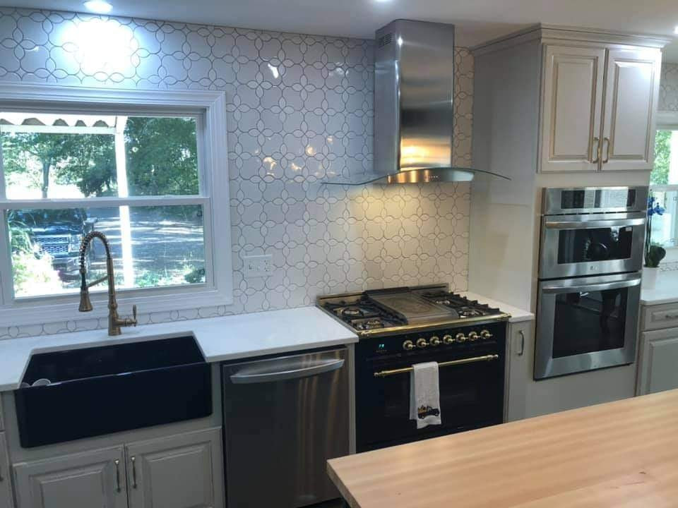 Mid-sized transitional l-shaped vinyl floor and brown floor kitchen photo in DC Metro with a farmhouse sink, raised-panel cabinets, gray cabinets, solid surface countertops, white backsplash, ceramic backsplash, stainless steel appliances, an island and white countertops