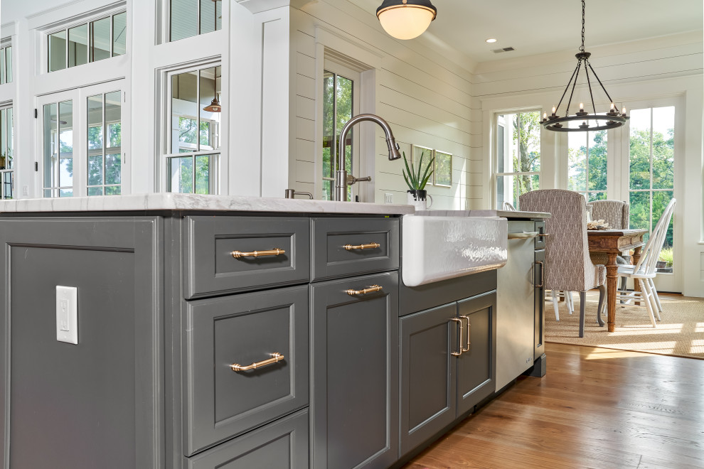 Large transitional l-shaped light wood floor and brown floor open concept kitchen photo with a farmhouse sink, flat-panel cabinets, gray cabinets, granite countertops, white backsplash, wood backsplash, stainless steel appliances, an island and white countertops