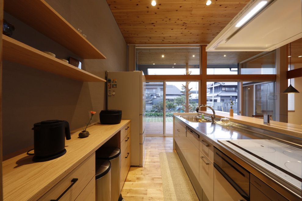 This is an example of a contemporary single-wall kitchen in Other with stainless steel benchtops, white splashback, medium hardwood floors and wood.