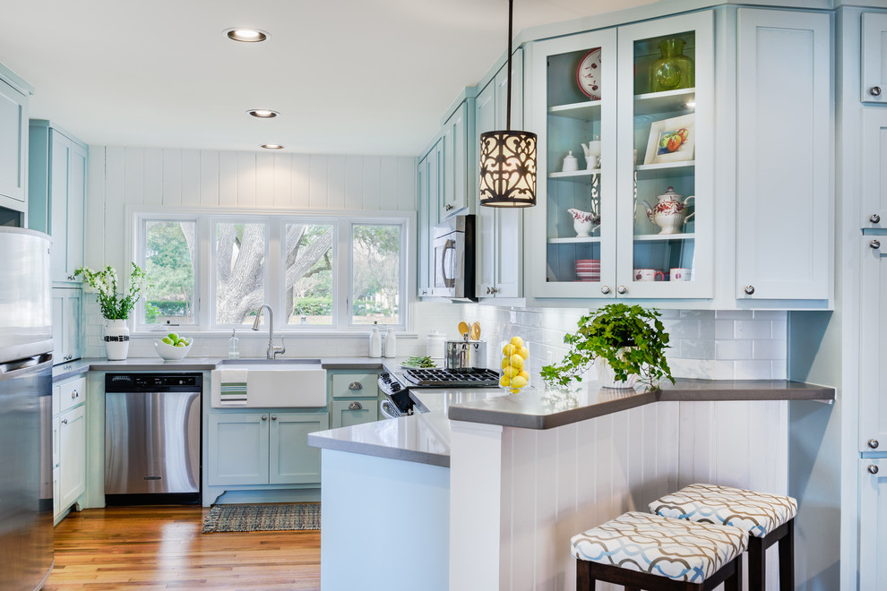 Traditional u-shaped eat-in kitchen in Austin with a farmhouse sink, shaker cabinets, blue cabinets, solid surface benchtops, white splashback, subway tile splashback, stainless steel appliances, medium hardwood floors and no island.