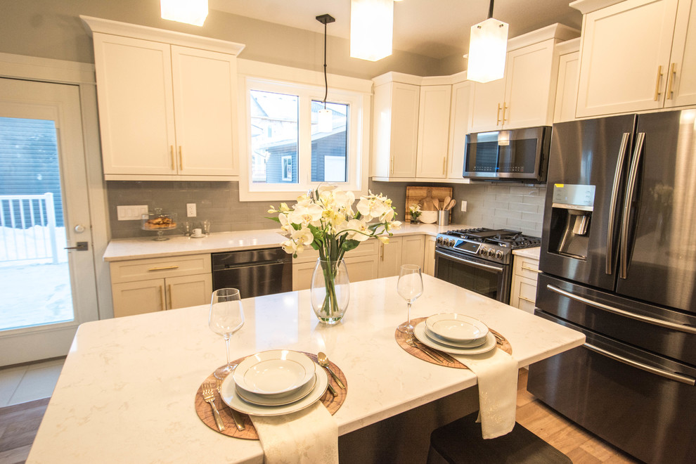 Inspiration for a large transitional l-shaped medium tone wood floor and brown floor enclosed kitchen remodel in Calgary with an undermount sink, shaker cabinets, white cabinets, marble countertops, gray backsplash, subway tile backsplash, black appliances, an island and white countertops