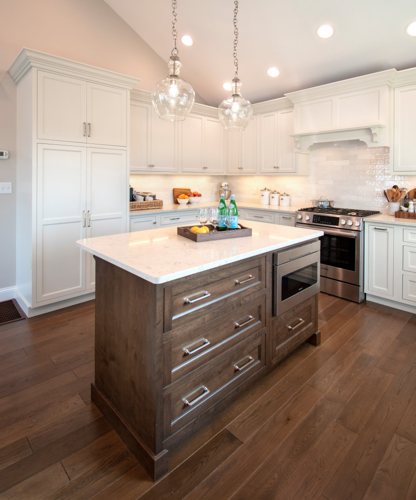 Example of a transitional medium tone wood floor, brown floor and vaulted ceiling eat-in kitchen design with shaker cabinets, white cabinets, quartz countertops, white backsplash, ceramic backsplash, stainless steel appliances, an island and white countertops
