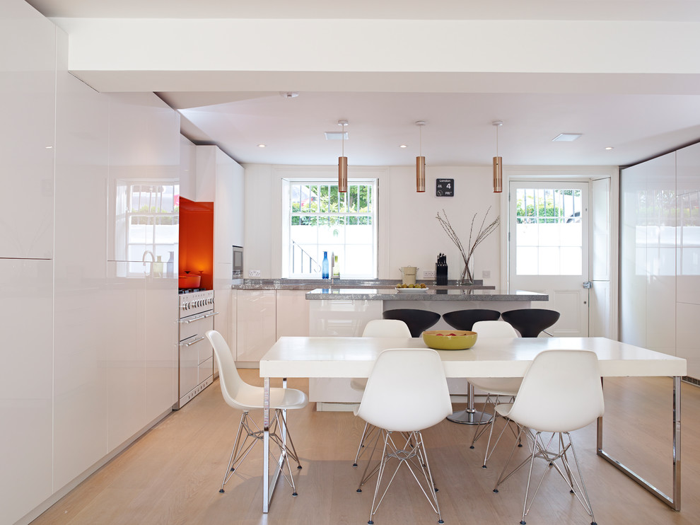 Inspiration for a mid-sized contemporary kitchen in London with flat-panel cabinets, white cabinets, solid surface benchtops, orange splashback, glass sheet splashback, white appliances and with island.