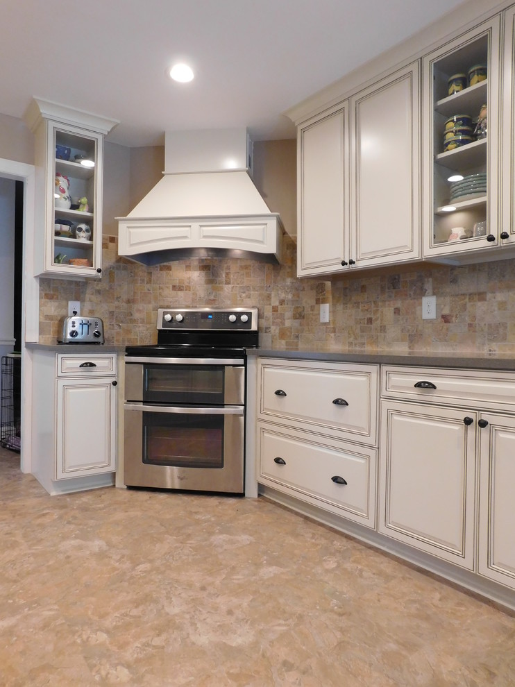 Example of a mid-sized transitional galley vinyl floor enclosed kitchen design with a farmhouse sink, raised-panel cabinets, beige cabinets, solid surface countertops, multicolored backsplash, stone tile backsplash, stainless steel appliances and no island