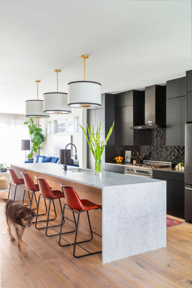 Design ideas for a mid-sized modern galley open plan kitchen in Denver with an undermount sink, flat-panel cabinets, black cabinets, marble benchtops, black splashback, ceramic splashback, stainless steel appliances, light hardwood floors, with island, beige floor and white benchtop.