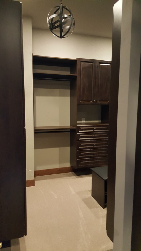 This is an example of an expansive traditional gender-neutral walk-in wardrobe in Seattle with raised-panel cabinets, dark wood cabinets, carpet and beige floor.