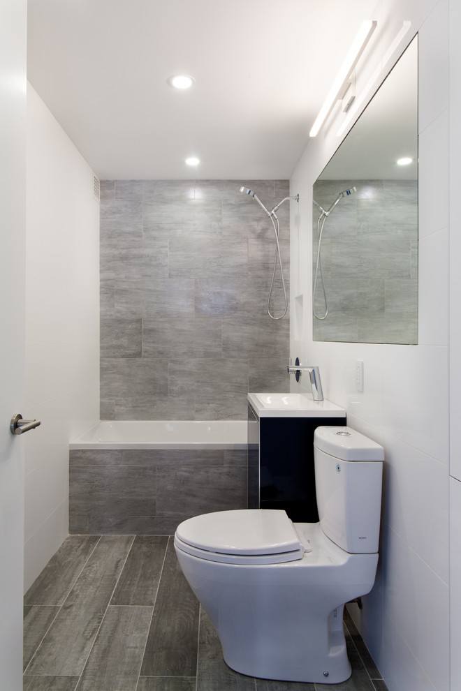This is an example of a small contemporary 3/4 bathroom in New York with flat-panel cabinets, black cabinets, an alcove tub, a shower/bathtub combo, a one-piece toilet, gray tile, porcelain tile, white walls, porcelain floors, a pedestal sink and solid surface benchtops.
