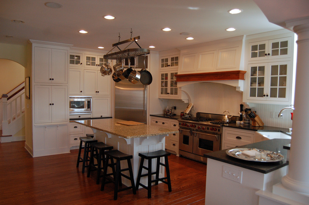 This is an example of a large traditional u-shaped eat-in kitchen in Milwaukee with a farmhouse sink, recessed-panel cabinets, white cabinets, white splashback, stainless steel appliances, medium hardwood floors, with island, granite benchtops and timber splashback.