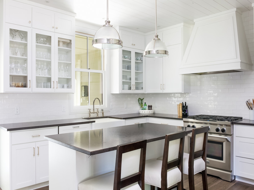 Inspiration for a transitional l-shaped dark wood floor and brown floor kitchen remodel in Austin with a farmhouse sink, glass-front cabinets, white cabinets, white backsplash, subway tile backsplash, stainless steel appliances and an island