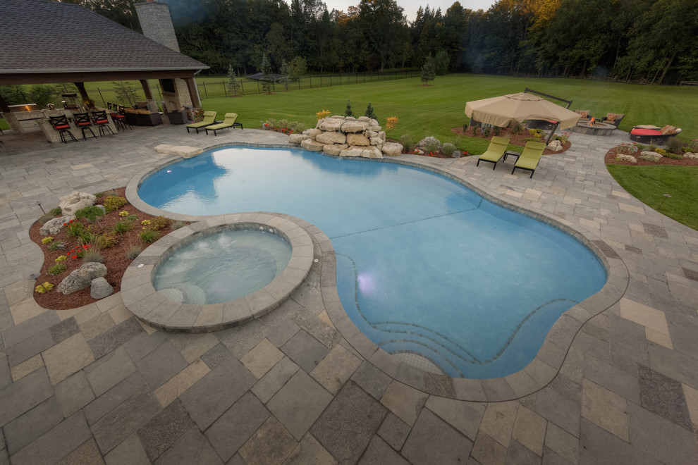 This is an example of a mid-sized contemporary backyard custom-shaped lap pool in Toronto with a hot tub and concrete pavers.