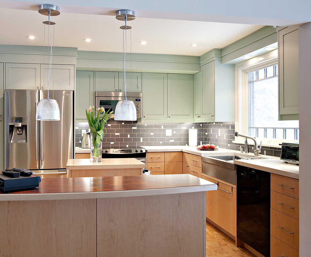 This is an example of a contemporary l-shaped kitchen in Toronto with a farmhouse sink, recessed-panel cabinets, green cabinets, grey splashback and black appliances.