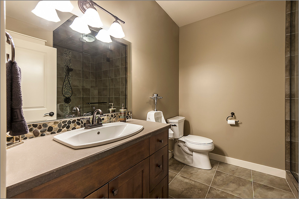 Inspiration for an expansive contemporary master bathroom in Calgary with a drop-in sink, recessed-panel cabinets, medium wood cabinets, solid surface benchtops, a curbless shower, an urinal, multi-coloured tile, stone tile, beige walls and ceramic floors.