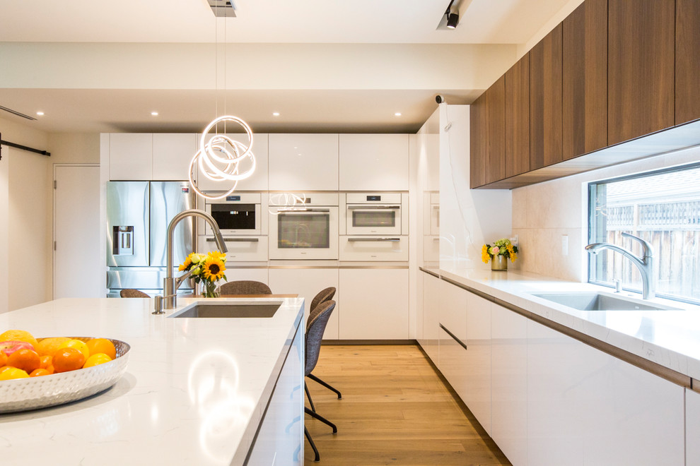 Photo of a mid-sized contemporary u-shaped eat-in kitchen in San Francisco with an undermount sink, flat-panel cabinets, white cabinets, quartzite benchtops, grey splashback, cement tile splashback, white appliances, medium hardwood floors, with island, brown floor and white benchtop.