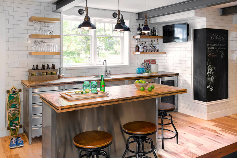 This is an example of an industrial galley seated home bar in Vancouver with a drop-in sink, open cabinets, wood benchtops, white splashback, subway tile splashback, medium hardwood floors and brown benchtop.