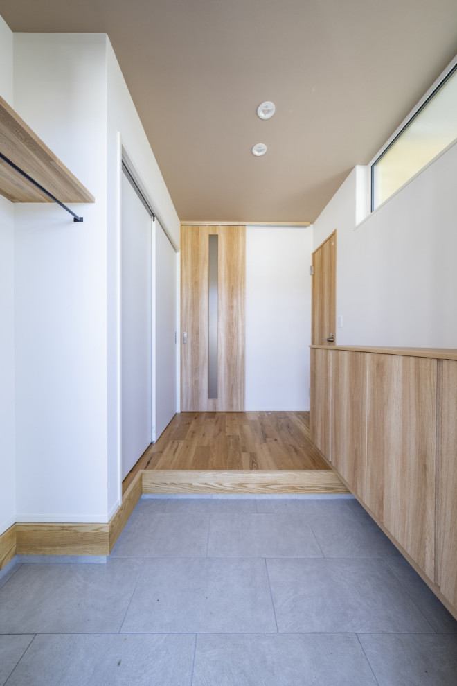 Modern inredning av en mellanstor hall, med vita väggar, ljust trägolv, en enkeldörr, ljus trädörr och brunt golv