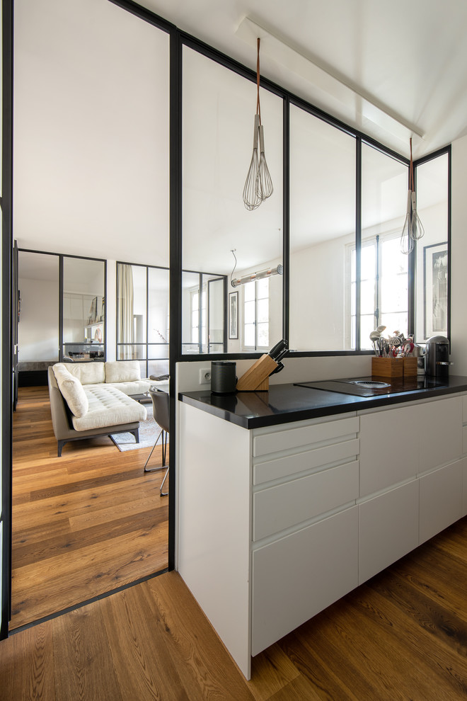 Small galley open plan kitchen in Paris with an undermount sink, beaded inset cabinets, white cabinets, quartzite benchtops, brown splashback, timber splashback, panelled appliances, dark hardwood floors, brown floor and black benchtop.