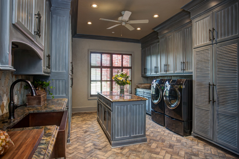 This is an example of a large traditional galley dedicated laundry room in Little Rock with a farmhouse sink, grey cabinets, granite benchtops, grey walls, brick floors, a side-by-side washer and dryer, beige floor and recessed-panel cabinets.