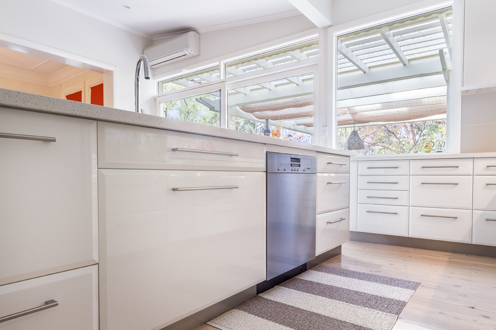 Design ideas for a large contemporary l-shaped open plan kitchen in Sydney with an undermount sink, white cabinets, solid surface benchtops, beige splashback, ceramic splashback, stainless steel appliances, light hardwood floors and with island.
