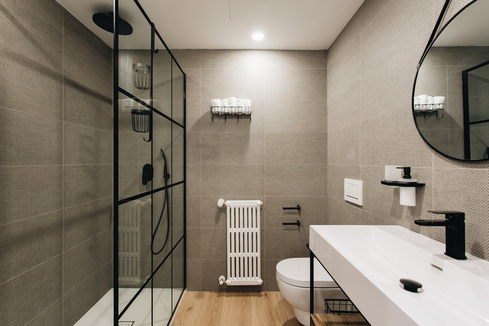 Inspiration for a large modern master bathroom in Valencia with furniture-like cabinets, medium wood cabinets, an alcove shower, a wall-mount toilet, brown tile, ceramic tile, brown walls, light hardwood floors, a trough sink, brown floor and white benchtops.