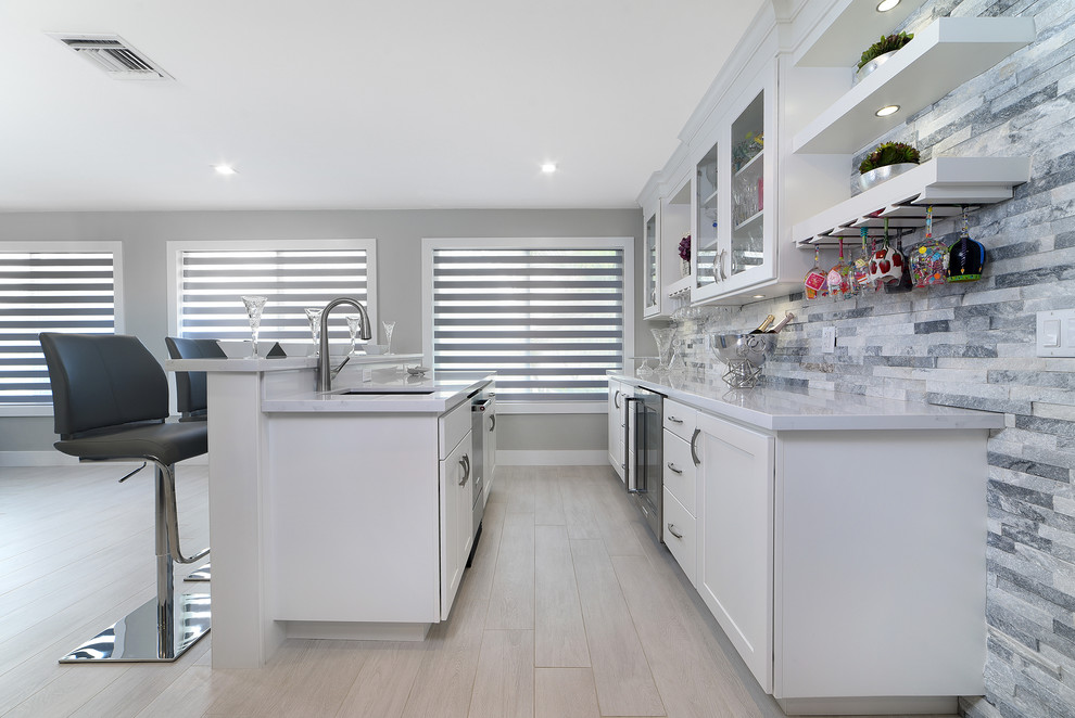 Open concept kitchen - large transitional l-shaped porcelain tile and gray floor open concept kitchen idea in Miami with a farmhouse sink, shaker cabinets, gray cabinets, quartz countertops, gray backsplash, marble backsplash, stainless steel appliances and two islands