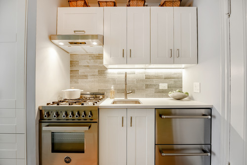 Small L-shaped studio kitchen with white shaker kitchen cabinet uppers, baskets above to use vertical space, under-cabinet lighting, and a compact range