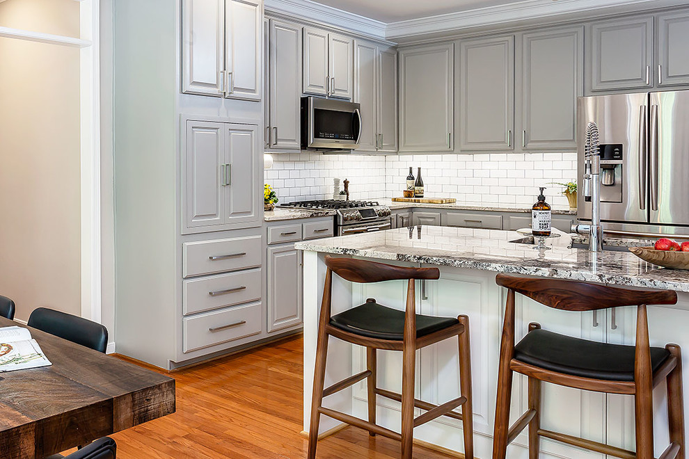 Inspiration for a mid-sized transitional l-shaped medium tone wood floor and brown floor eat-in kitchen remodel in Richmond with a farmhouse sink, gray cabinets, granite countertops, white backsplash, ceramic backsplash, stainless steel appliances, an island and multicolored countertops