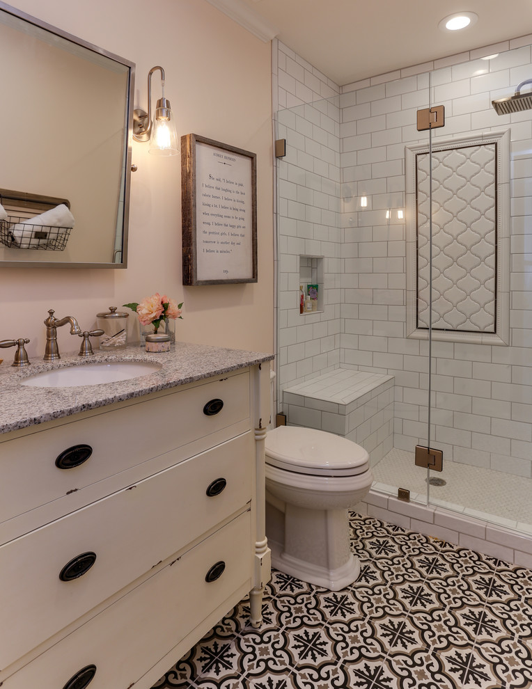 Photo of a small transitional 3/4 bathroom in Raleigh with distressed cabinets, white tile, an undermount sink, granite benchtops, furniture-like cabinets, an alcove shower, a two-piece toilet, subway tile, beige walls, concrete floors, multi-coloured floor and a hinged shower door.