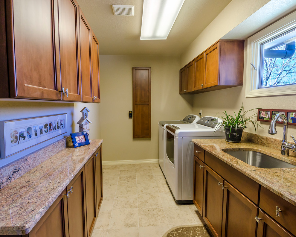 This is an example of a large traditional galley dedicated laundry room in Denver with an undermount sink, recessed-panel cabinets, dark wood cabinets, granite benchtops, beige walls, ceramic floors and a side-by-side washer and dryer.