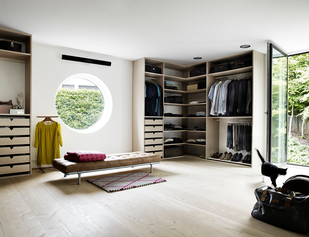 This is an example of a large contemporary gender-neutral dressing room in London with flat-panel cabinets, light wood cabinets, light hardwood floors and beige floor.